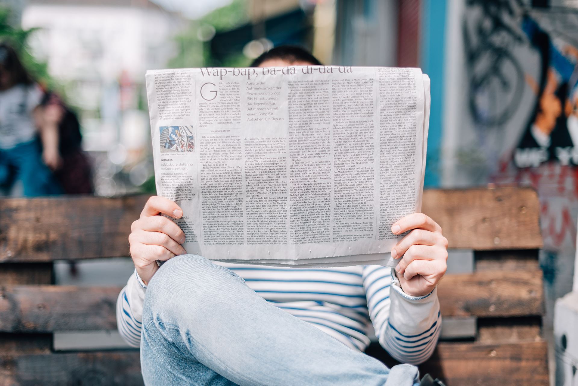 Picture of a person sat on a bench reading a newspaper